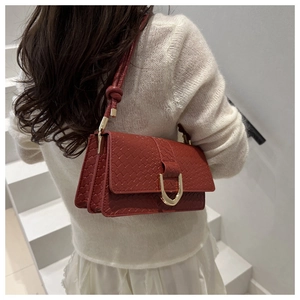 Detail of dark red textured baguette bag featuring a gold horseshoe metal clasp and strap