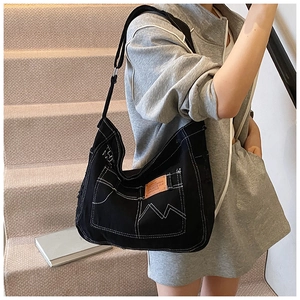 Detail of black canvas tote bag showing white contrast stitching and utility pocket