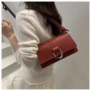 Detail of red-brown crocodile embossed handbag featuring a gold horseshoe buckle clasp