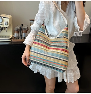 Close-up of colorful striped woven tote bag with adjustable cream shoulder strap on a model