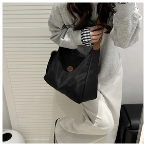 Detail of black nylon tote bag featuring brown leather logo and adjustable wide strap