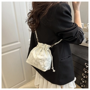 Detailed view of white butterfly lace bucket bag with pearl strap on model shoulder