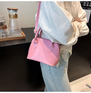 Side view of a pink matte shell bag with handle and adjustable shoulder strap worn with style