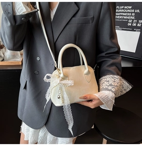 Close-up of mini white shell bag featuring lace bow and pearl charm on gray suit