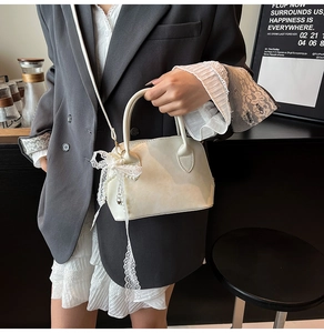 Detail of a creamy white lace shell bag with pearl pendant and bow decoration