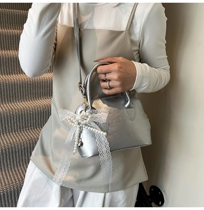 Close-up of a silver metallic shell bag with lace bow and pearl charm detailing
