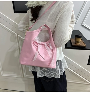 Detailed view of a pink leather tote bag featuring a large white lace bow and a shoulder strap