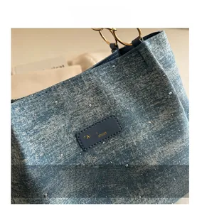 Detail of blue denim textured handbag with silver rhinestones and gold handle ring