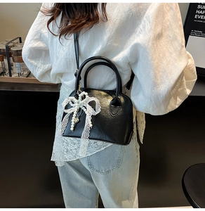 Close-up of black shell bag featuring lace pearl bow charm and leather texture on a model