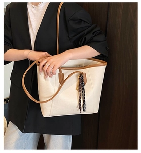 Detail of cream bucket bag with brown straps and striped knot charm on model
