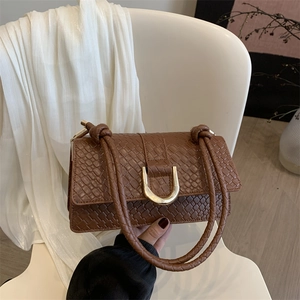 Brown woven shoulder bag with golden U-shaped buckle on a white chair stylish texture