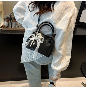 Close-up of black shell bag with lace pearl bow and heart charm on a model