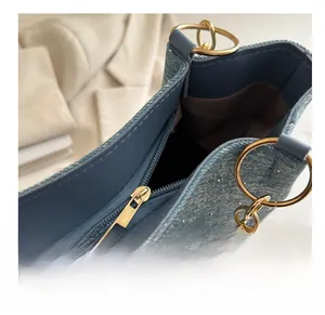 Detail of blue denim tote bag featuring a smooth gold zipper and brown fabric lining