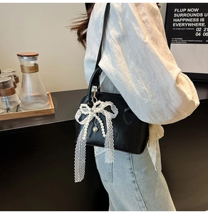 Detail of black shell bag featuring a delicate white lace bow and pearl bead charm