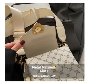 Détail d'un fermoir magnétique doré en forme de cœur sur un sac bandoulière crème