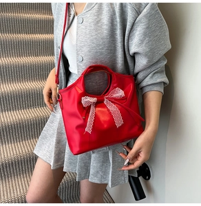 Detail of red tote bag with white lace bow and adjustable strap on a gray background