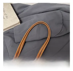 Detail show of rounded brown leather handle with precision stitching on a tote bag