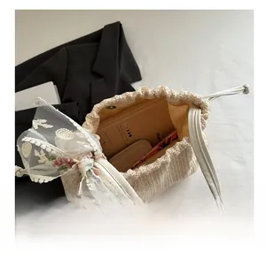 Draufsicht auf eine beige Stroh-Beuteltasche mit floraler Spitzenschleife und Stauraum