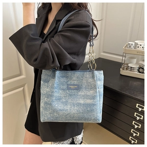 Detail of light blue denim tote bag with metallic chain strap and leather brand patch