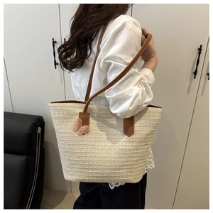 Detail of hand-woven straw tote with brown leather straps and pink butterfly charm