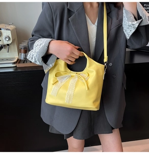 Yellow tote bag with white lace bow detail, held by a model in a casual cafe setting