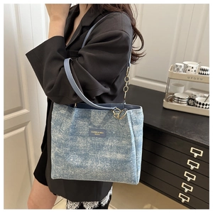 Detail of light blue denim tote bag with leather logo patch and gold chain strap