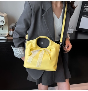 Detail view of a bright yellow handbag featuring a white lace bow on smooth faux leather