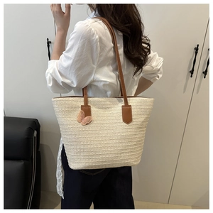 Detail view of woven straw tote bag with brown leather strap and pink lace butterfly