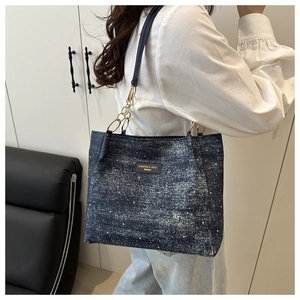 Detail of blue denim tote bag with white pearl studs and gold chain strap attachment