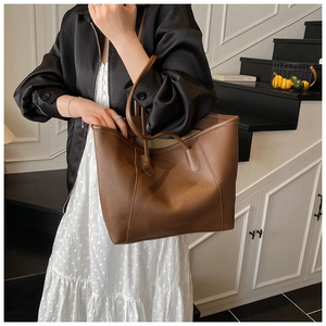 Detail of brown lychee texture leather tote bag with subtle logo and long strap handles