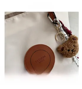 Macro shot of beige fabric tote featuring a round leather logo and brown plush bear charm