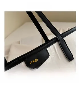 Close-up of white textured tote bag featuring a black leather tag with golden text