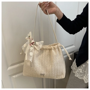 Detail der beigen Strohtasche mit weißer Spitzenschleife und metallischem Anhänger