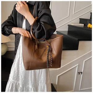 Close-up of a large brown tote bag with litchi texture and woven tassel pendant detail