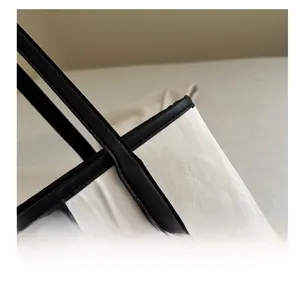 Detail of white wrinkled fabric tote with black leather trim and gold logo stitching