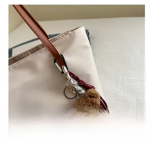 Close-up of a brown plush bear charm with gold ring attached to a beige tote bag