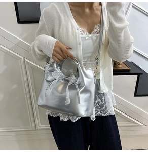 Detail of silver metallic leather tote bag featuring a white lace bow and chain strap