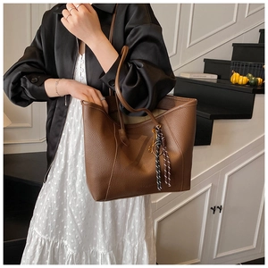 Close-up of brown lychee grain leather tote bag with stylish braided tassel detail
