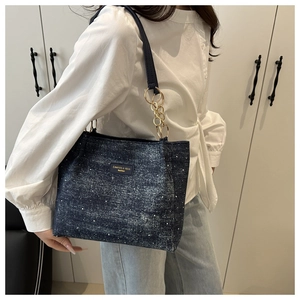 Detail of dark blue denim tote bag with starry effect and gold chain strap on shoulder