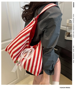 Detail of red striped canvas tote bag with white lace bow on shoulder of model