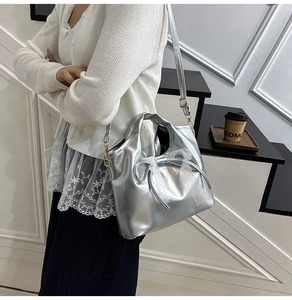 Detalle del bolso plateado de cuero encerado con lazo de encaje blanco y bandolera