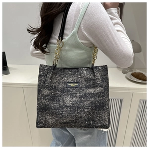 Detail of grey-black textured tote bag featuring gold-tone chain and leather logo patch