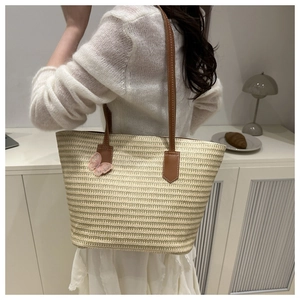 Detail of straw woven tote with leather handles and a pink butterfly charm accessory