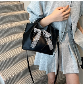 Detalle de un bolso de mano negro brillante con un gran lazo de encaje blanco suave