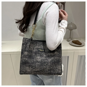 Close-up of textured tote bag with golden chain strap and brand logo detail