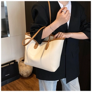 Close-up of cream pebble-grain tote bag with brown leather handles and embossed logo