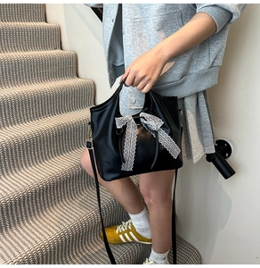 Detail of black glossy leather handbag featuring a white lace bow and adjustable strap
