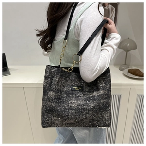 Detail of tweed tote bag with sequins and leather strap worn by a model in casual setting