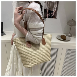 Détail d'un cabas en paille tissée avec anses en cuir marron et accent papillon rose