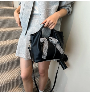 Detail of black faux leather bag featuring a delicate white lace bow and gold hardware